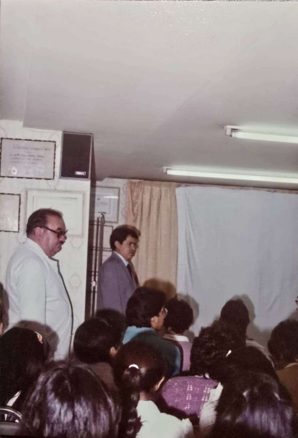 Profesor Dr. Francisco Arellano Ocampo enseñando dermatología a jóvenes médicos en formación en la Clínica Dermatológica de Puebla, con diplomas de la Universidad Autónoma de Puebla visibles al fondo. Maestro formador de generaciones de dermatólogos en Puebla.